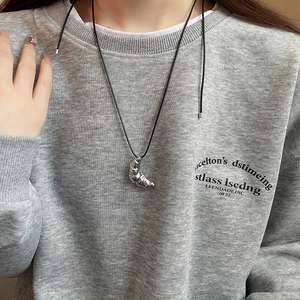 Close-up of a silver croissant pendant on a black cord necklace worn with a grey hoodie
