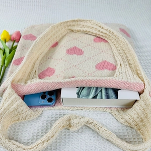 Beige knit tote bag with pink hearts showing capacity for smartphone and books