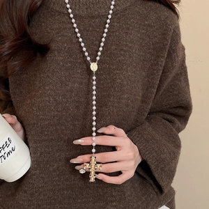 Detail of vintage pearl necklace with golden medal and jeweled cross pendant on brown sweater