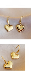 Close-up of golden heart drop earrings on beige silk fabric with high mirror finish