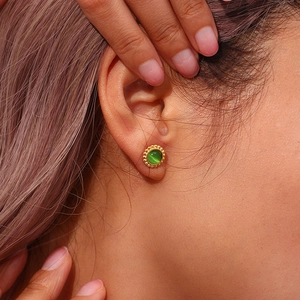 Close-up of golden sun-shaped earring with green cat-eye stone worn on a model's ear
