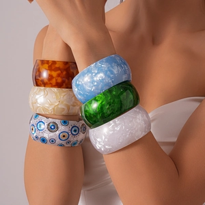 Close-up of stacked iridescent acrylic geometric cuff bracelets in amber and marble tones