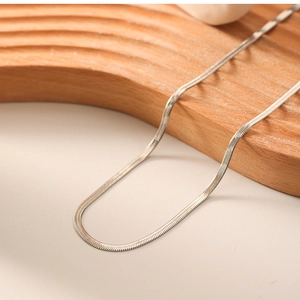 Detailed close-up of a silver flat snake bone chain necklace on a curved wooden stand