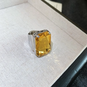 Close-up of a large rectangular yellow gemstone ring with a silver setting and faceted cut