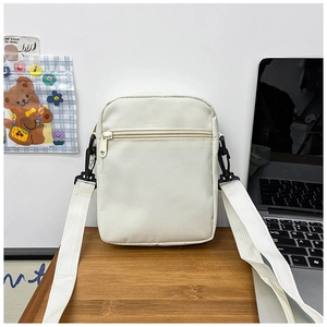 Detailed view of an off-white canvas crossbody bag on a wooden desk with office supplies