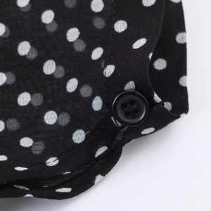Dettaglio del tessuto nero a pois che mostra un bottone rotondo e trama leggera