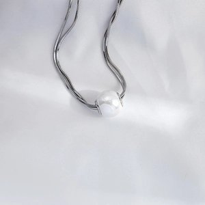 Macro detail of a polished white pearl on a sleek silver-tone snake chain necklace