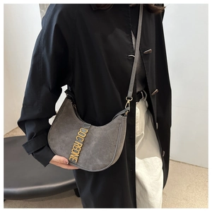 Detail of grey suede crescent shoulder bag with golden metal logo and long strap