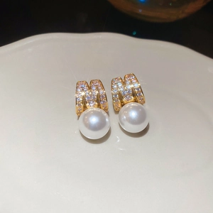 Close-up of golden M-shaped earring with sparkling zircons and white pearl pendant