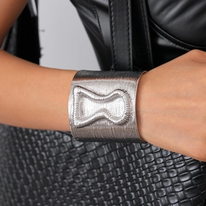 Close-up of silver wide open bangle featuring hourglass relief and brushed metal texture