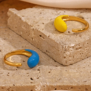 Detail of colorful enamel teardrop rings on beige stone, adjustable gold design