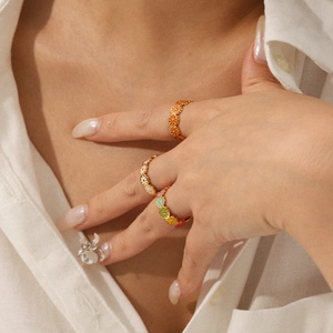 Close-up of colorful enamel daisy rings layered on model fingers with golden finish