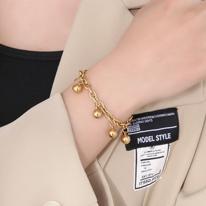 Close-up of polished gold spherical charms on a link chain bracelet worn by a model