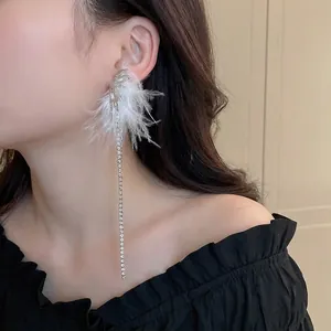 Asymmetric silver feather earrings with sparkling rhinestone tassels worn by a model