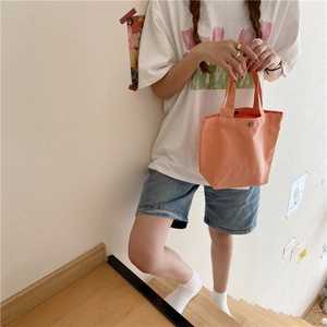 Detail of a small orange canvas tote bag with metal snap button in a lifestyle setting