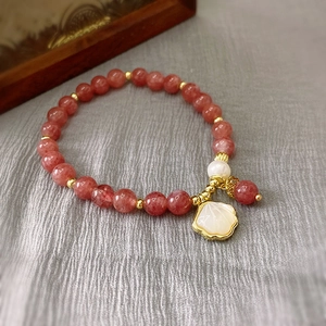 Close-up of strawberry quartz beaded bracelet with a pearl and gold shell pendant
