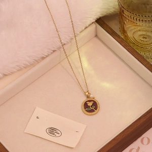 Detail of vintage gold rose pendant necklace with small pearl and green enamel accents