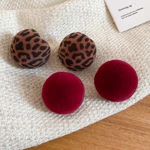 Close-up of leopard print and deep red flocked round earrings on a knit fabric surface