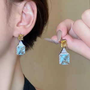 Detailed close-up of geometric earrings with blue and yellow stones and silver micro-pave