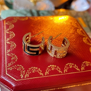 Close-up of asymmetrical gold C-shaped earrings with Greek key patterns on a red gift box