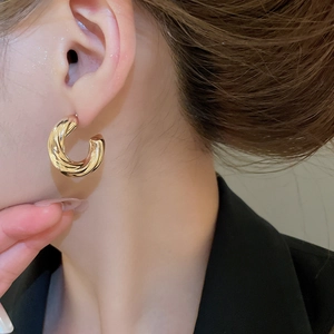 Detailed view of golden C-shaped hoop earrings with twisted spiral texture on model