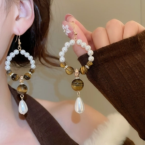 Detail of vintage earrings with tiger eye stone and drop pearl on golden metal hooks