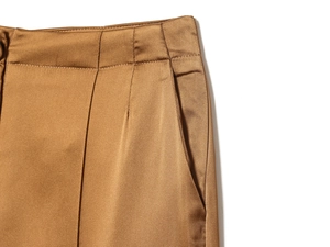 Detailed view of bronze satin wide-leg pants showing waist pleats and side pockets