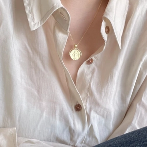 Close-up of gold 925 sterling silver coin necklace on woman wearing a linen shirt