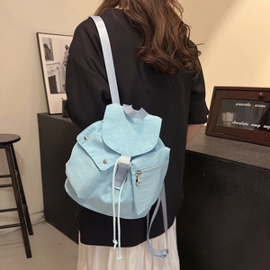 Detail view of a light blue nylon backpack featuring a drawstring and flap closure design