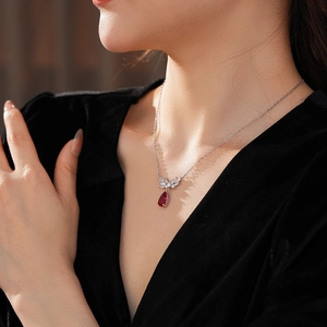 Macro view of silver necklace featuring a red teardrop pendant with winged detail for women