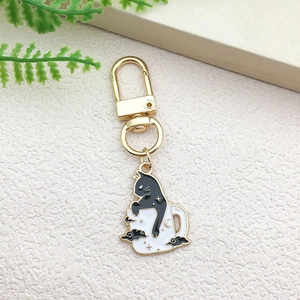 Cartoon black cat sitting on a white mug charm keychain with gold metal d-ring