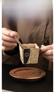 Detail of square ceramic cup with hand-painted daisy and wooden coaster and stirrer