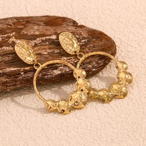 Macro detail of 18K gold-plated earrings with hammered texture on a rustic background