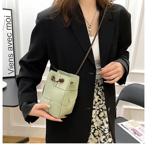 Detail of hand-woven light green bucket bag with drawstring closure and slim strap