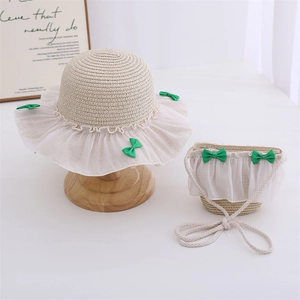 Detail of kids straw hat and matching bag with white lace trim and green bows