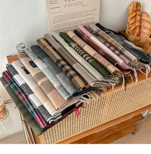 Stack of checkered cashmere-feel scarves with tassels in multiple colors on a wooden cabinet