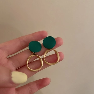 Detail of hand-held retro earrings with dark green studs and matte gold rings