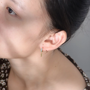Close-up of gold feather earrings with turquoise stone worn by model in a side view