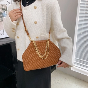 Brown quilted crossbody bag with gold chain strap styled on a model in a white coat