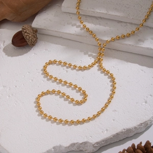 Minimalist gold bead chain necklace displayed on natural stone and autumn leaves