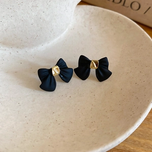 Close-up of elegant black matte bow earrings with golden center on ceramic plate