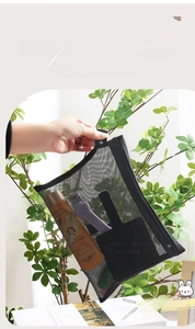 Handheld view of a black mesh storage bag featuring a woven strap for travel toiletries
