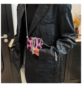 Close-up of pink leopard print mini bag with silver chain strap on black textured blazer