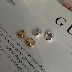Polished gold and silver arched huggie earrings displayed on a fashion magazine page