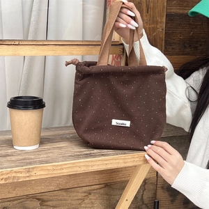 Close-up of dark coffee polka dot drawstring bag with Sozakka tag on wooden shelf