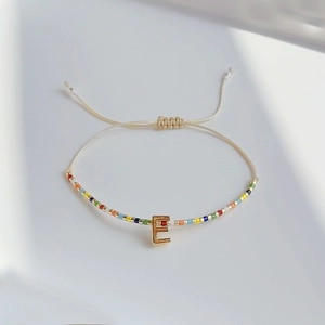 Detail eines verstellbaren Regenbogen-Perlenarmbands mit goldenem 3D-Buchstaben E