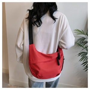 Detail view of red nylon tote bag with wide black strap worn by model in casual style