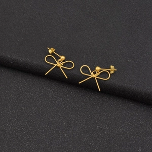 Macro shot of gold bow-shaped earrings with round beads on a black textured background