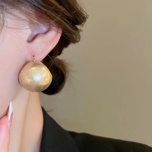 Detail view of large matte champagne gold U-shaped ball earring on a female model