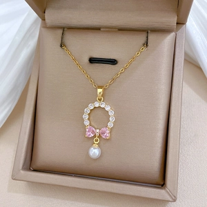 Detailed macro view of gold necklace with pink heart bow and pearl pendant on silk